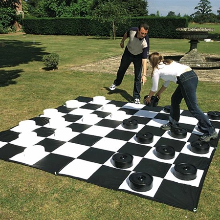 A man and a woman playing checkers on a giant board in a park.