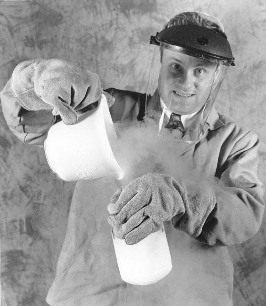 A man, wearing protective gear, pouring liquid nitrogen into a glass jar.