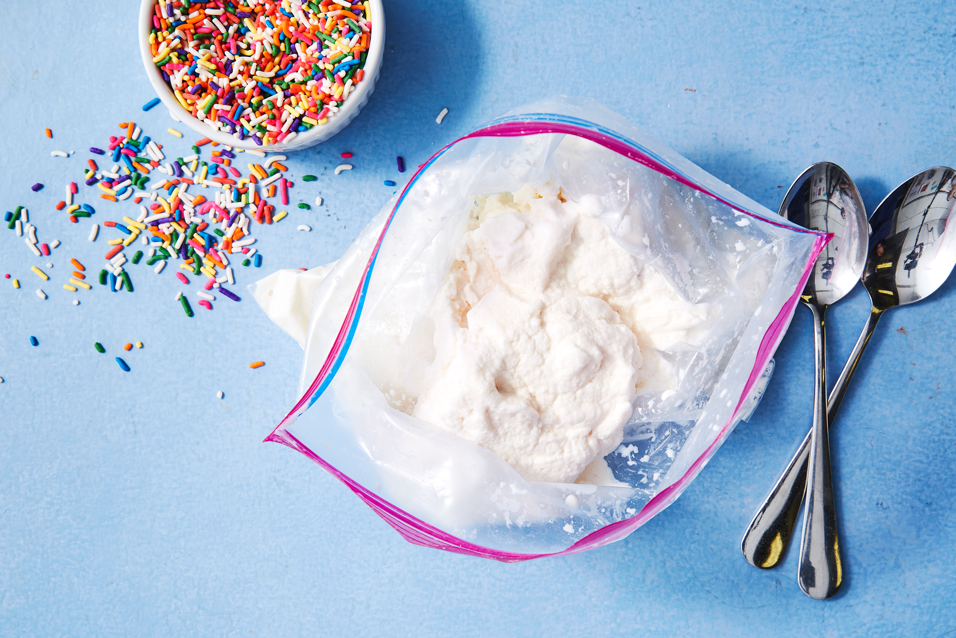 Ice cream in a plastic bag, two spoons, and a jar of sprinkles
