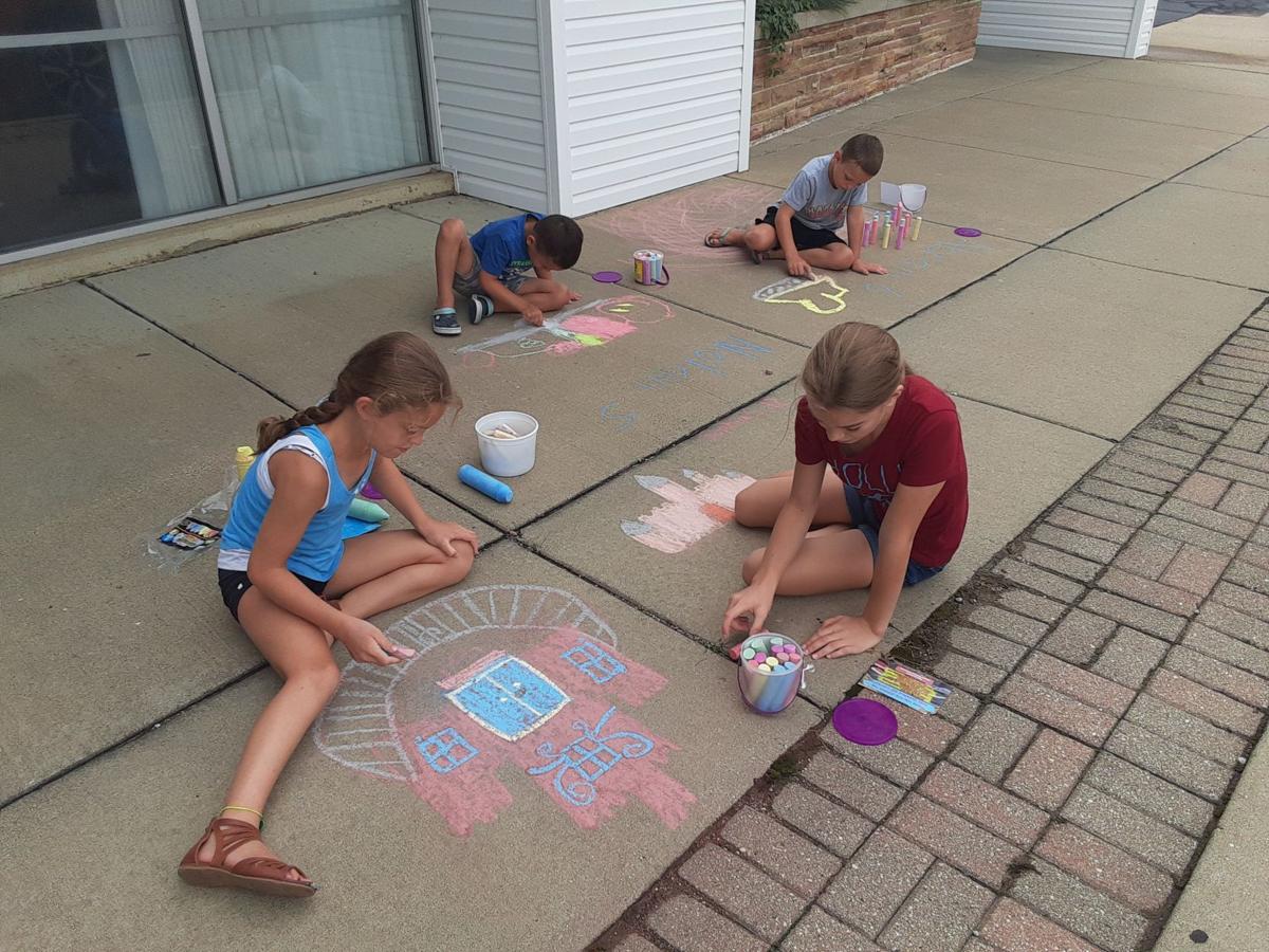 Four kids drawing with chalk on the sidewalk.
