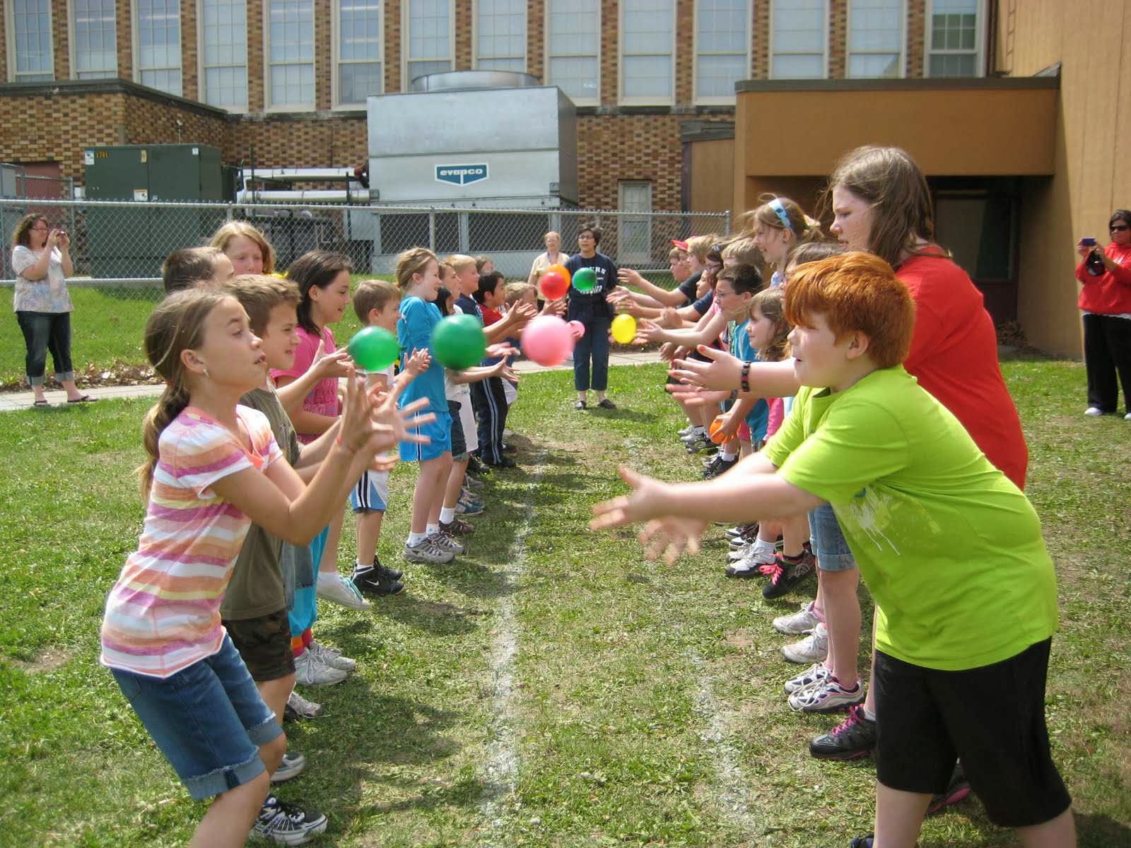 Boys and girls, standing in two lines, tossing water balloons to each other.