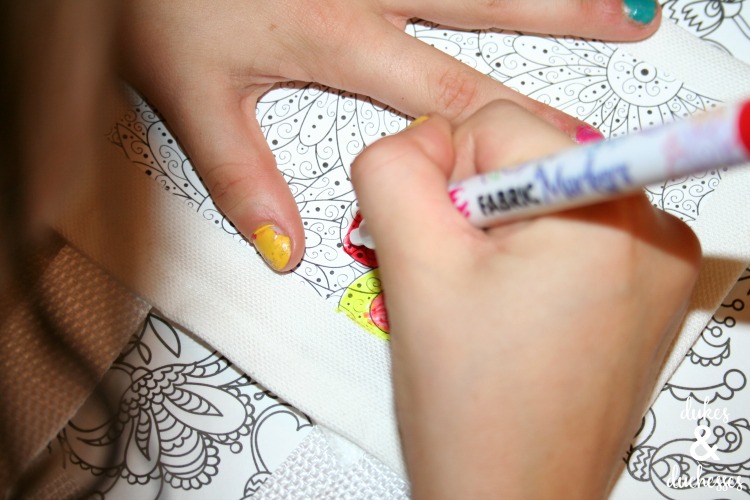 Two hands coloring a tote bag with markers.