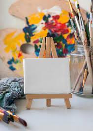 A small canvas on a tiny easel.  Paintbrushes are in the background in a mason jar.