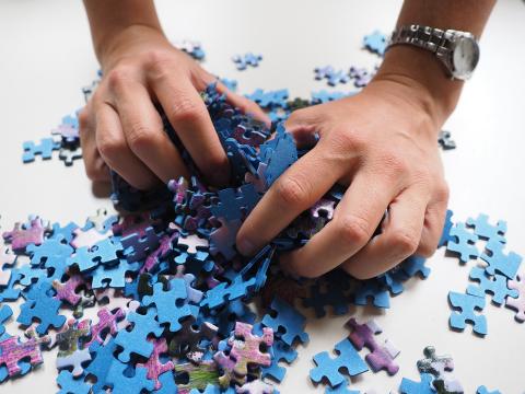 A man's two hands, grasping at a pile of puzzle pieces.
