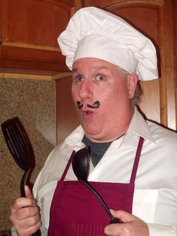 A man holding a spatula and wearing a chef's hat and apron