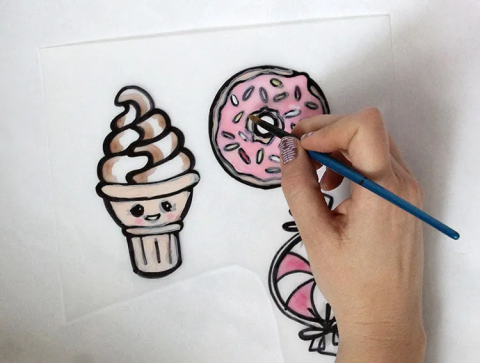 A hand drawing a doughnut on Shrinky Dink plastic.