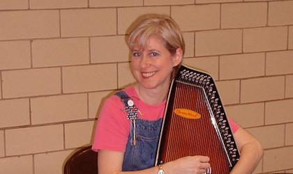 A light-haired woman holding a dulcimer.