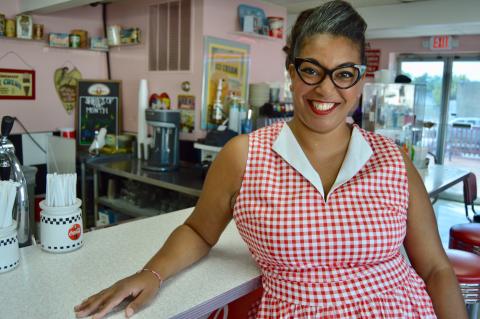 Woman with glasses, smiling and leaning on a counter.