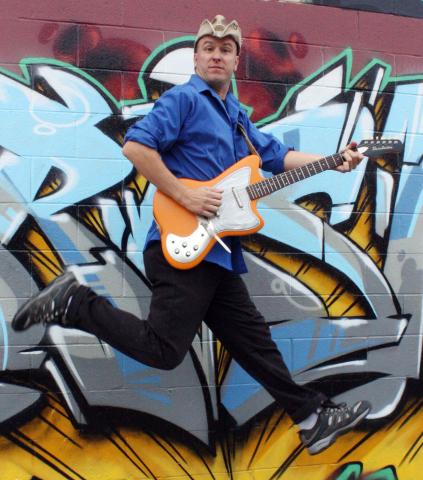 Man wearing a cowboy hat, holding a guitar and leaping sideways