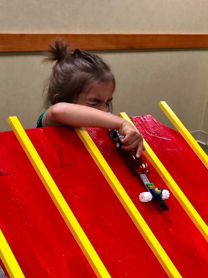 Boy putting his lego car on a wooden race track.