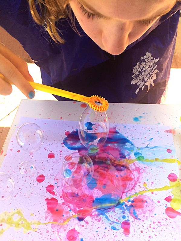 Young girl blowing colored bubbles onto paper.