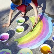 Boy painting a rainbow on the sidewalk with chalk paint