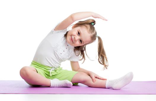 A little girl sitting and stretching on a yoga mat.